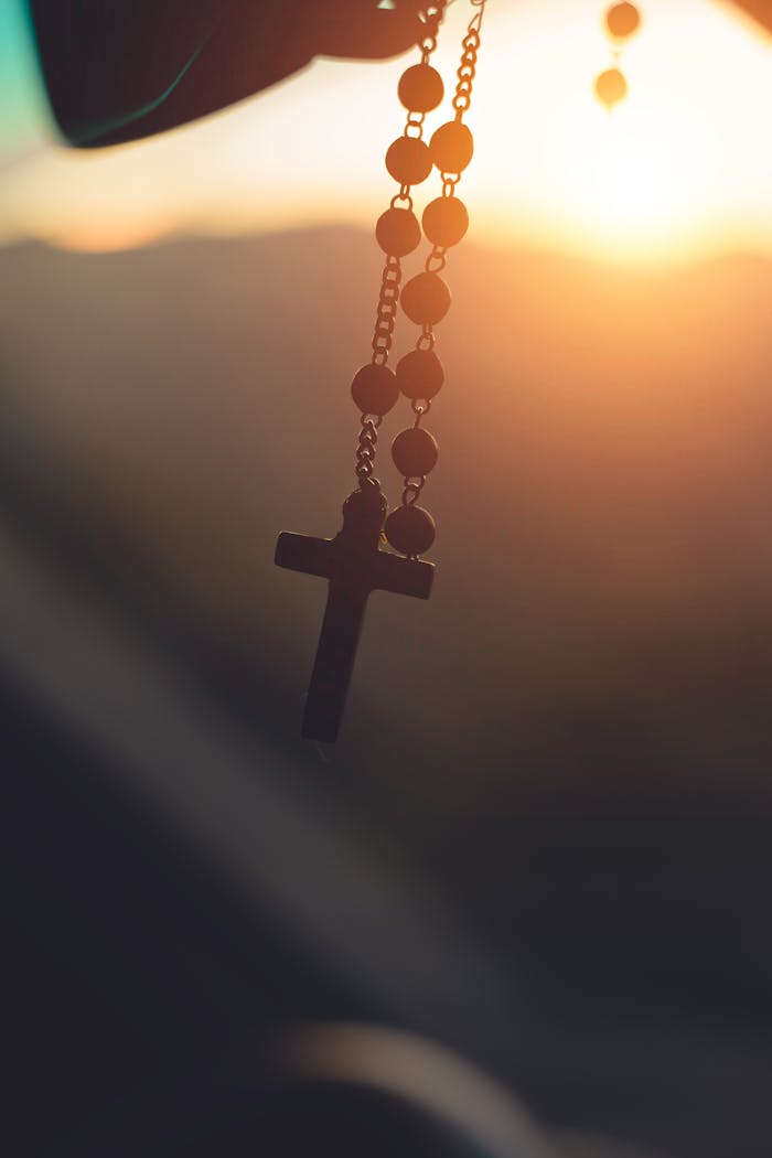 Silhouette of a rosary cross hanging with sunrise background in Brazil, capturing spiritual serenity.